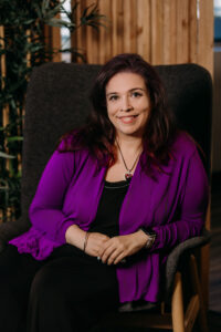 Image of Karly Stein sitting in chair, wearing a purple and back top.